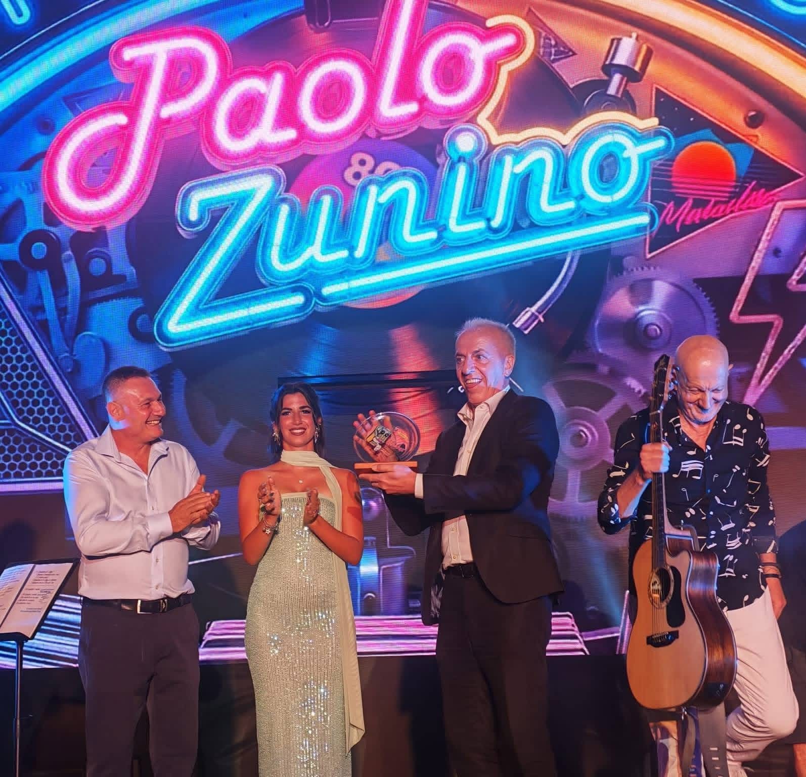 Andora 2026 — Paolo Zunino riceve il Premio Speciale «Jukebox in Satira» nell’ambito della manifestazione «Tutti nel Jukebox», con Marco Carena e il presentatore e organizzatore Luca Galtieri sul palco.